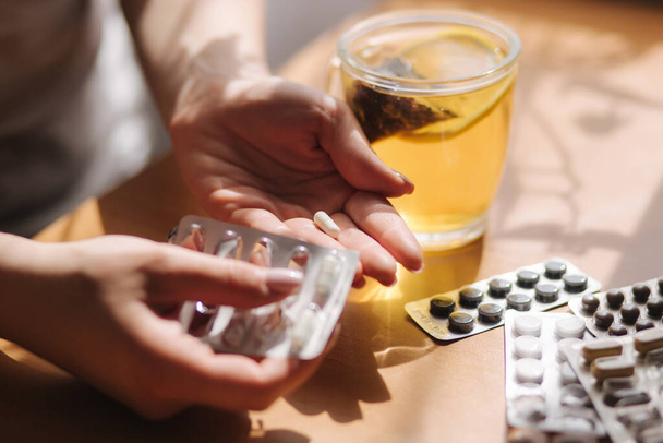 Close up of womans hands hold pills. Hand with pills and black tea with lemon. Immunity. Vitamines - Photo, Image