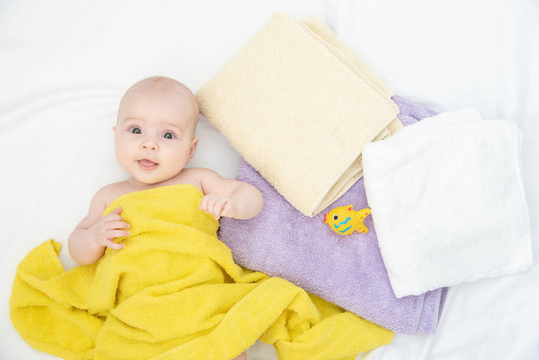 Portrait of a beautiful cheerful little baby in a yellow towel after bath on a white cloth - Photo, Image