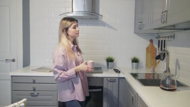 Young woman pours and drinks coffee at home in kitchen - Séquence, vidéo