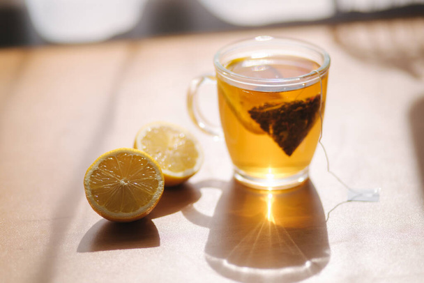 Černý čaj s citrónem na dřevěném stole. Čajový sáček s plátkem citronu v šálku - Fotografie, Obrázek
