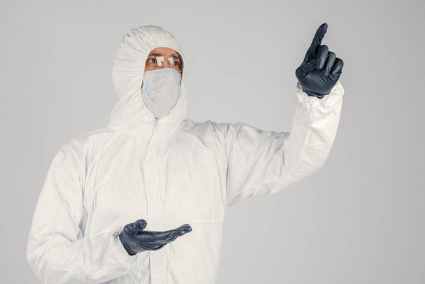 Ludzki epidemiolog w jednorazowym antyepidemicznym kombinezonie antybakteryjnym pokazuje gesty dłoni na białym tle. Epidemia i pojęcie medyczne. - Zdjęcie, obraz