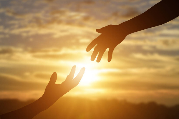 Σιλουέτα δίνοντας ένα χέρι βοήθειας, ελπίδα και υποστήριξη ο ένας τον άλλον κατά τη διάρκεια ηλιοβασίλεμα φόντο. - Φωτογραφία, εικόνα