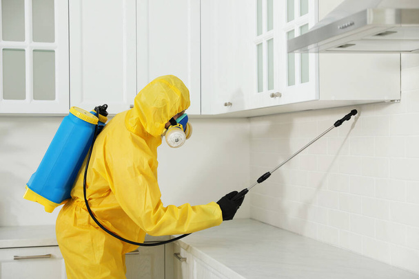 Pest control worker in protective suit spraying insecticide on furniture indoors - Foto, Imagem