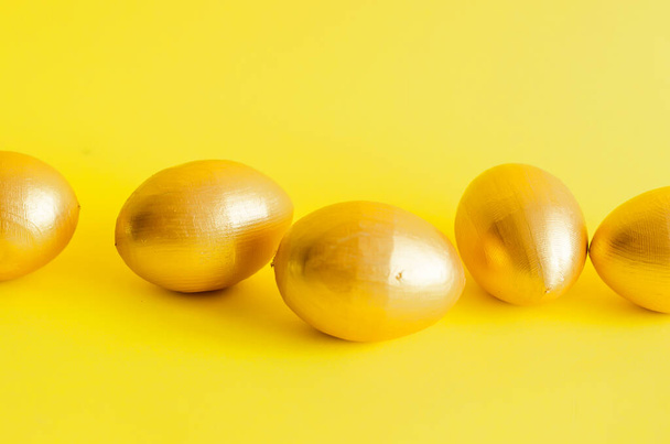 gold decorative eggs rolling  and knock each other a yellow background. Spring holiday concept. Copy space, template mockup Easter greeting card  - Foto, Imagem