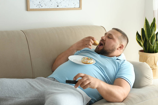 Lazy overweight man with donuts watching TV on sofa at home - Фото, зображення
