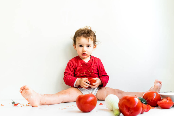 Ein barfüßiges Baby beißt auf rote Tomaten und schmiert seinen Saft. - Foto, Bild