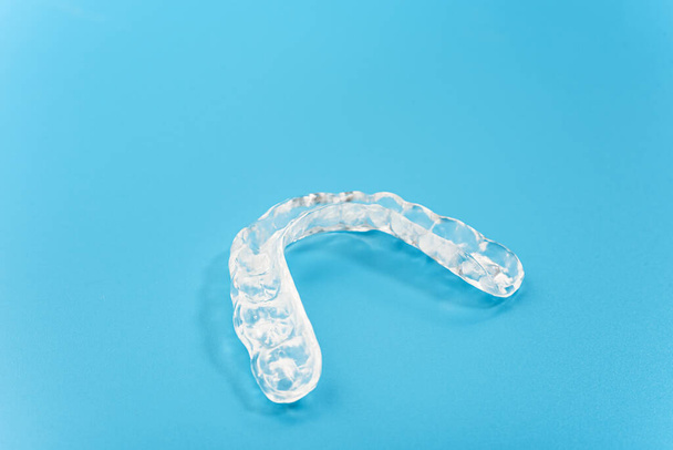 青色の背景に隔離された歯科医師によって使用される歯科用アライナー. - 写真・画像