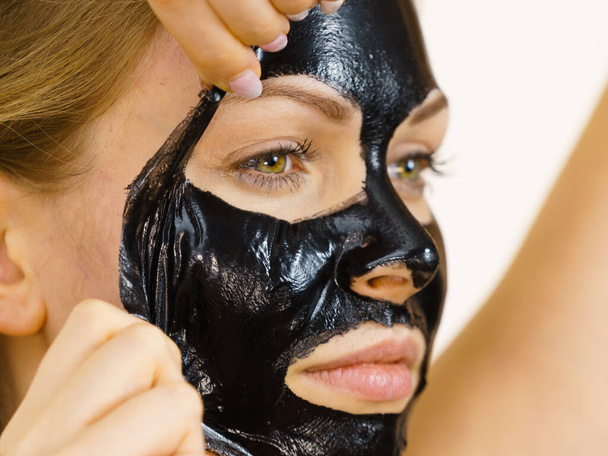 Young woman removing carbo black peel-off mask from her face, on white. Teen girl taking care of oily skin, cleaning the pores. Beauty treatment. Skincare. - Фото, изображение