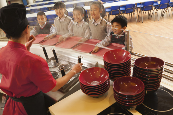Trabajador de cafetería de la escuela sirve fideos a los estudiantes
 - Foto, Imagen