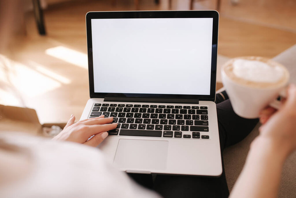 Вид від першої особи на жінку, що працює вдома. Жінка працює на ноутбуці і п'є капучино. Макет, білий екран. Карантинний час
 - Фото, зображення