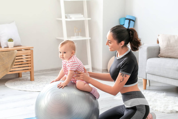 Joven madre deportiva y su bebé haciendo ejercicios con fitball en casa
 - Foto, imagen