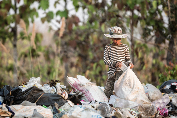 Fakir bir çocuk varoşlardaki bir çöp sahasından çöp topluyor. Çocuklar geçimlerini sağlamak için bu sitelerde çalışıyorlar. Yoksulluk kavramı. - Fotoğraf, Görsel