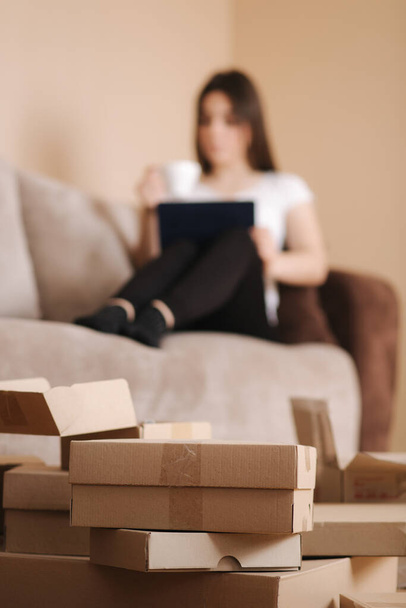 Woman shopping online at home use tablet. Woman work on tablet and drink cappuccino. Quarantine time. Boxes on the floor. Parcel - Photo, Image