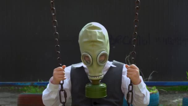 Beyaz takım elbiseli adam kafasına koruyucu lastik yeşil gaz maskesi takıyor ve derin derin nefes alıyor. Adam, Covid-19 virüsünden karantina nedeniyle metal zincirle salıncakta sallanıyor.. - Video, Çekim