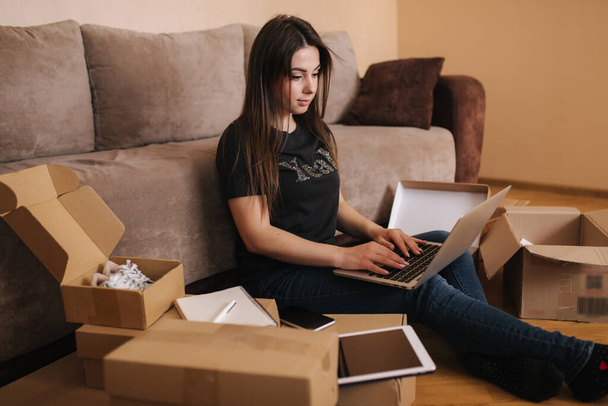 Happy young woman shopping online. Woman use laptop and tablet for searching new goods. Attractive girl surrounded by parcels - Photo, Image