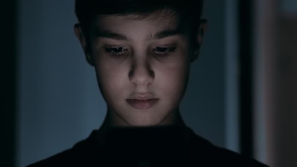 Close-up portret van schattige jongen van 10 jaar oud maakt gebruik van een smartphone 's nachts thuis. - Video