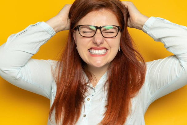 Jeune fille folle en colère dans des lunettes se tient par la tête sur un fond de mur jaune. Concept de stress, migraine et apathie
. - Photo, image