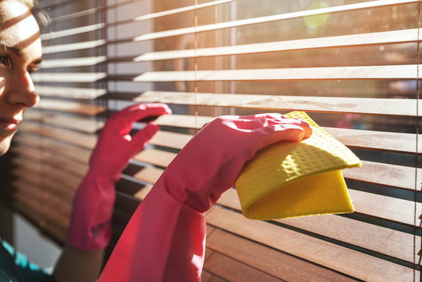 Женщина чистит деревянные окна жалюзи от пыли дома в солнечный день
 - Фото, изображение