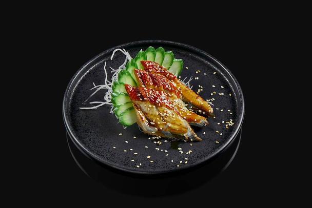 Classic raw eel sashimi with daicon raddish on a stylish black ceramic plate on a black background. Japanese traditional food. Photo for the menu - Foto, afbeelding
