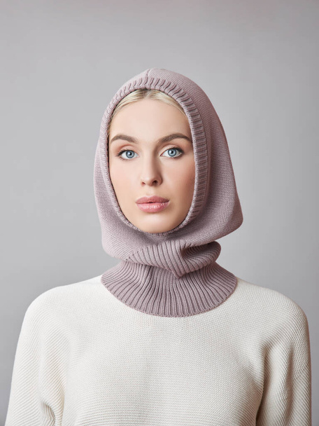 European Muslim woman with a blonde hair in a bonnet hood dressed on her head. Beautiful girl in sweater with soft skin, natural cosmetics - Fotó, kép
