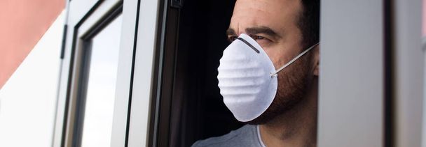 Man with face mask and gloves looking out the window. Stay at home concept. Panorama photo. - Foto, imagen