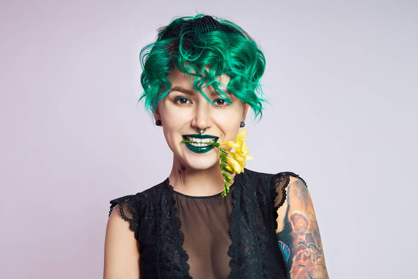 Woman with creative green coloring hair and makeup, toxic strands of hair. Bright color curly hair on the girl head, professional makeup. Woman with tattoo - Zdjęcie, obraz