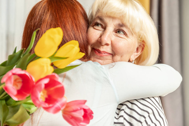 Moeder en dochter knuffelen elkaar. Dochter feliciteert moeder en geeft een boeket tulpen bloemen. Gelukkige Moederdag. - Foto, afbeelding