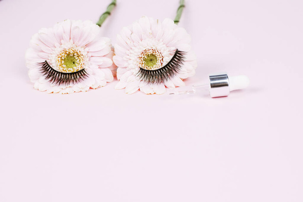 Flowers in the form of human eyes with eyelashes next to a pipette with moisturizing serum for the skin around the eyes. medical equipment and eye drop. - Photo, image