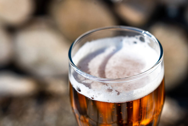 Cerveza ligera en un vaso de vidrio sobre el fondo de leña. Descanse en el campo. Espuma de cerveza a la luz del sol. - Foto, Imagen