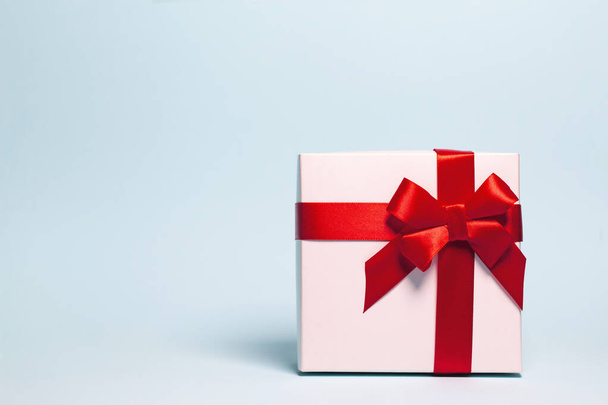 Παρόν κουτί τυλιγμένο με κόκκινη κορδέλα σε παστέλ φόντο. Εορταστικό και εορταστικό θέμα. Χριστούγεννα ή δώρο γενεθλίων. Έννοια πωλήσεων και αγορών. - Φωτογραφία, εικόνα