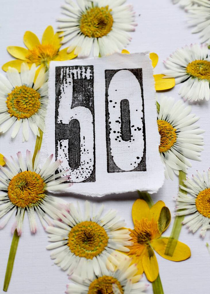 50歳の誕生日カードのイメージは、 50番の白い紙にスタンプ、押された春の花、黄色と白のデイジーと少ないセランディンの境界と。自然からインスピレーションを受けた、新鮮な花の背景画像  - 写真・画像