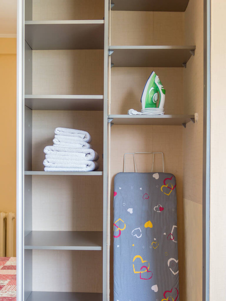 Tábua de engomar, ferro, toalhas limpas no armário
 - Foto, Imagem