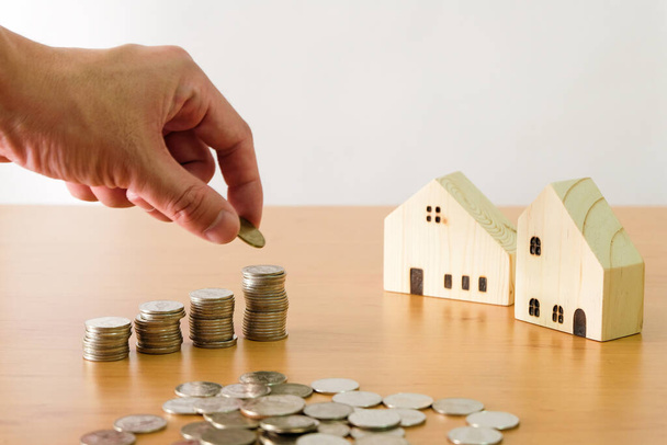 Selective focus Men hand puting coin on stack of money coin for saving for home, property with small wood house on the background. Wealth and saving plan for house mortgage Personal investment concept - Photo, Image
