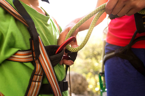 The instructor teaches the child to use climbing equipment, The boy is preparing to climb a rock, A woman shows a child how to use a carabiner for belaying, Mother ties the rope to the safety system. - Photo, Image