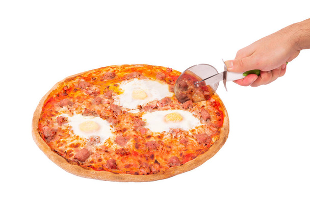 Pizza savoureuse avec des saucisses de bœuf, des œufs et du bacon ou pizza Brunch. main de l'homme avec un coupe-pizza couper la pizza isolée sur fond blanc avec chemin de coupe, vue d'angle
 - Photo, image