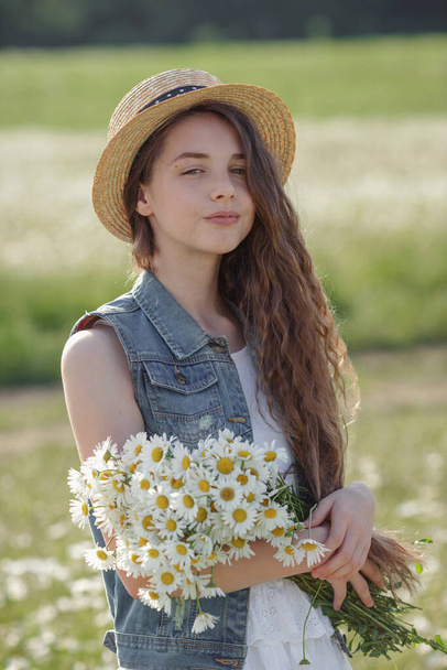 Schöne Teenager-Mädchen in einem weißen Kleid und Hut zu Fuß in einem Feld von Kamillen. Schönes langes und gesundes Haar. Die Idee und das Konzept der Gesundheit und Allergien, die Pflege für sich selbst - Foto, Bild