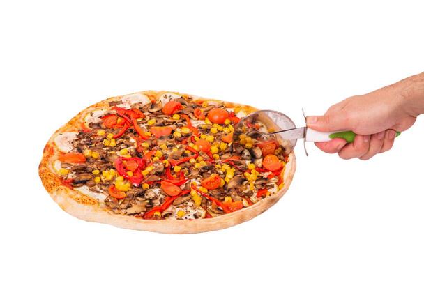 Gustosa pizza con funghi, mais, pomodorini ciliegia, zucchine e peperoni o Veggie pizza vegetariana. Mano dell'uomo con un tagliapizze tagliare la pizza isolata su sfondo bianco, vista ad angolo
 - Foto, immagini