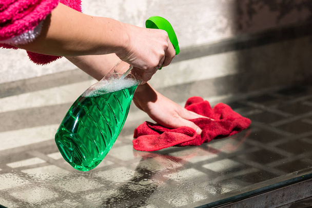 Mujer limpieza mesa de vidrio alfombra de microfibra roja y pulverizador de limpieza, concepto de servicios de limpieza. Concepto de trabajo doméstico y limpieza
 - Foto, imagen