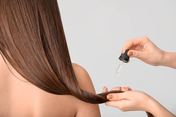 Applying of cosmetics on woman's hair against grey background - Fotografie, Obrázek