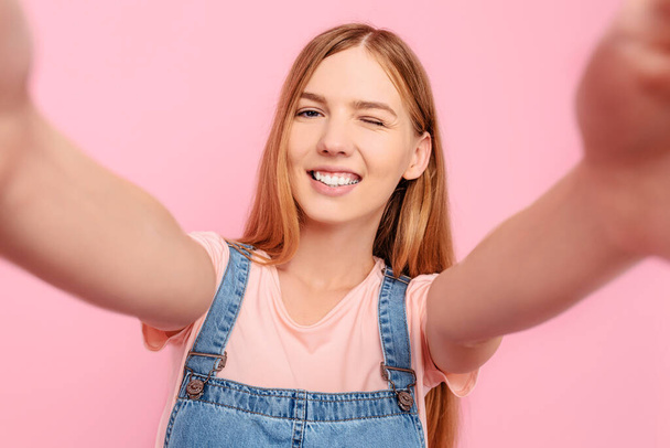 An attractive young stylish woman takes a selfie on her smartphone on an isolated pink background - Fotoğraf, Görsel