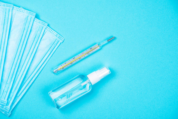 Draufsicht auf zwei chirurgische Einweg-Gesichtsmasken mit antibakteriellen antiseptischen Sprays für Händedesinfektionsmittel und Thermometer auf blauem Hintergrund. Schutz vor Viren. Kopierraum - Foto, Bild
