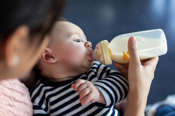 Close-up of mother feeding her baby son with feeding bottle while sitting on sofa at home. - Valokuva, kuva