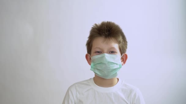 Happy handsome kid with short hair in gray long sleeve in mask smile, laugh and take off the mask with pleasure on white background. Little boy enjoy life despite the quarantine and isolation period. - Footage, Video