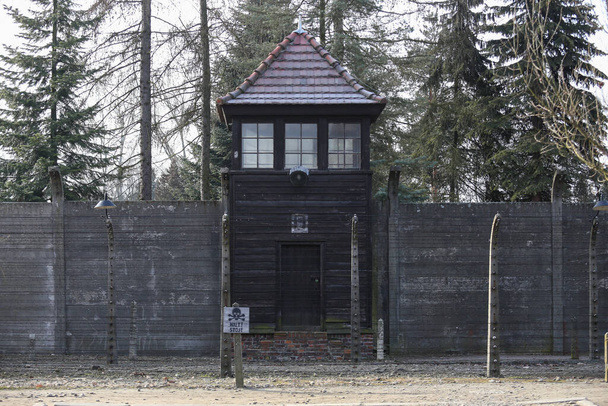 Auschwitz, Oswiecim, Poland - 27 January 2020: Part of Auschwitz Concentration Camp Holocaust Memorial Museum, electric fence with barbed wire and watch tower, Arbeit Macht Frei - Фото, изображение