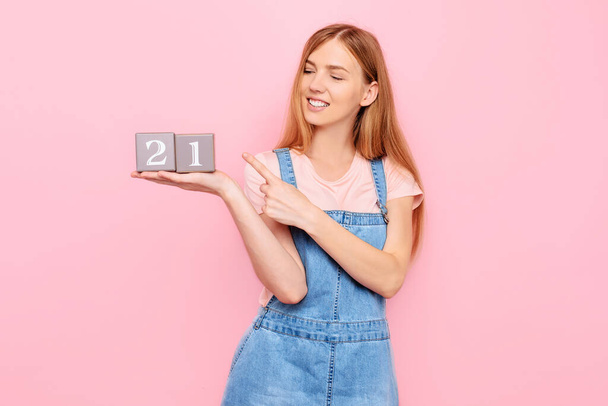 A fun cute young girl is celebrating her birthday and holding cubes with her age 21 twenty- one, on an isolated pink background - Valokuva, kuva
