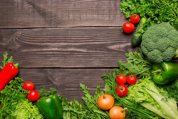 Frame van felgroene en rode verse groenten op houten achtergrond, bovenaanzicht, kopieerruimtePeper, broccoli, sla, arugula, peterselie, wortel - Foto, afbeelding