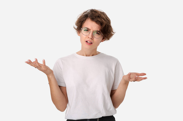 Prise de vue en studio d'une jeune femme désemparée portant une chemise blanche et des lunettes haussant les épaules en regardant la caméra en perte de vitesse. Concept de doute, d'incertitude et de confusion
 - Photo, image