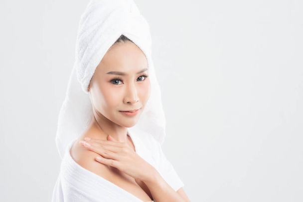 Όμορφη νεαρή γυναίκα σε πετσέτα μπάνιου αγγίζει το πρόσωπό της και χαμογελά απομονωμένη σε λευκό φόντο. Γυναίκα μετά το μπάνιο με καθαρό τέλειο δέρμα. - Φωτογραφία, εικόνα