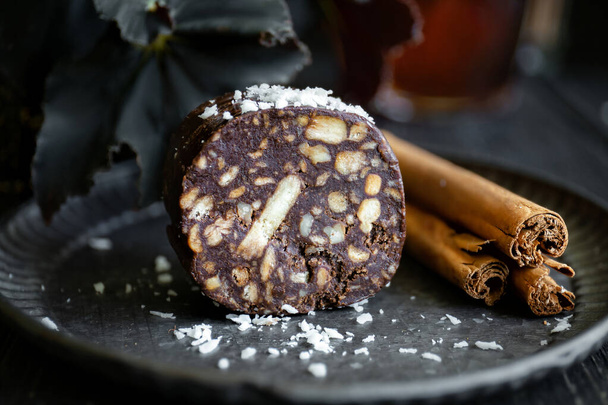 Stuk chocolade salami bestrooid met kokos- en kaneelstokjes op metalen plaat, close-up - Foto, afbeelding