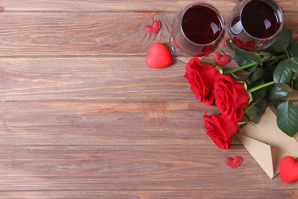 Κόκκινο κρασί, καρδιές, κόκκινα τριαντάφυλλα και δώρα σε έγχρωμο φόντο. - Φωτογραφία, εικόνα